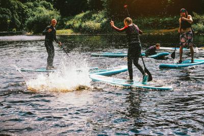 610686090 Group of teenagers having fun during a paddleboarding class. They are all laughing at one person who has fallen in, making a big splash.