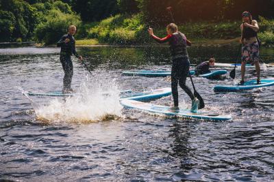 Group of teenagers having fun during a paddleboarding class. They are all laughing at one person who has fallen in, making a big splash.