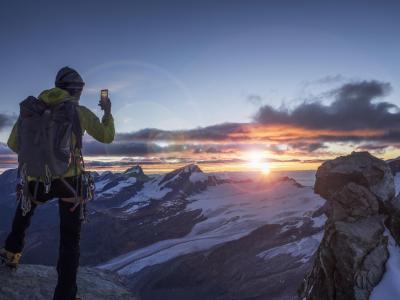 A climber on a mountain top taking pictures of a spectacular sunrise with his smartphone.