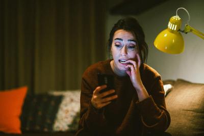 Lady sitting on her sofa looking worried at her phone.