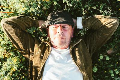 A mature man with his eyes closed enjoying the sunset lying on the grass in the field. Concept vacation, summer, happiness, lifestyle, mental health and wellness
