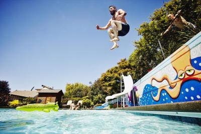 520749707 Man jumping from wall into outdoor pool with friends watching in background