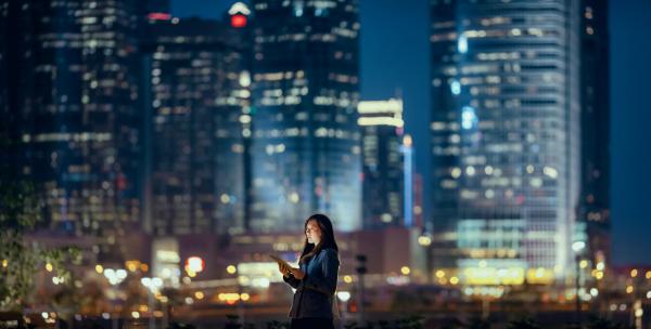 Young businesswoman using digital tablet in financial district, against illuminated corporate skyscrapers at night