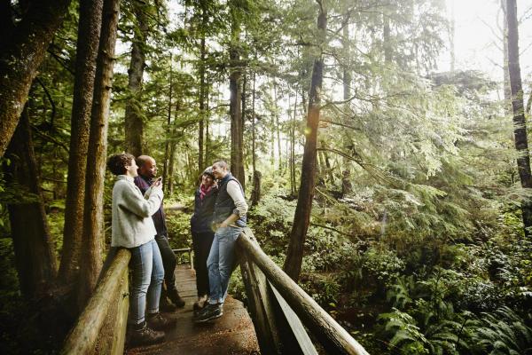 608167083 Woman taking digital photo with smartphone of couple while hiking on bridge in rainforest